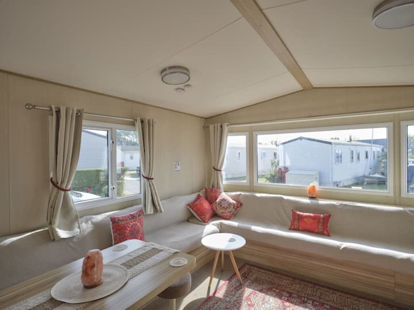 Interior acollidor d'una caravana amb un sofà, una taula petita i una finestra que mostra cases properes.