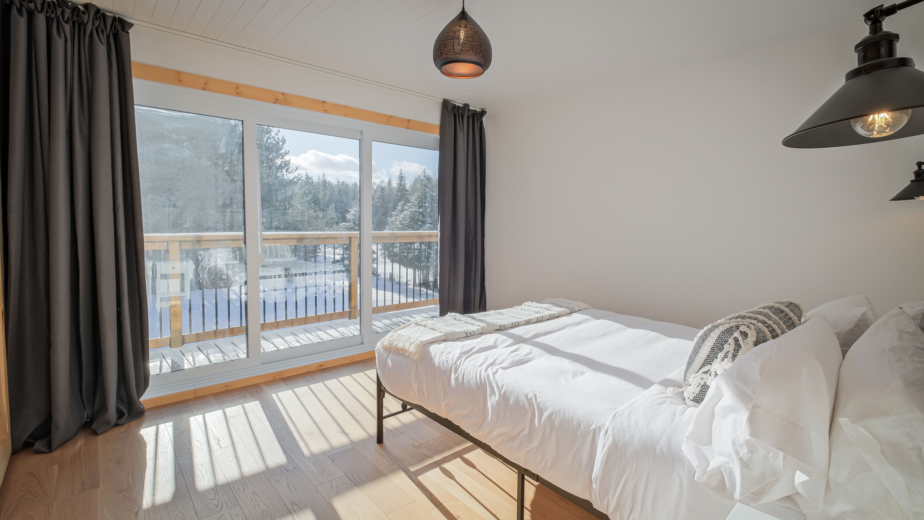 Une chambre avec une grande fenêtre, un lit et un luminaire suspendu.