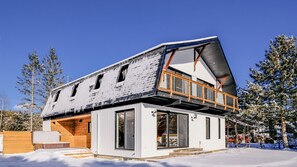 Una casa moderna de dos pisos con techo inclinado, ventanas amplias y una terraza de madera.