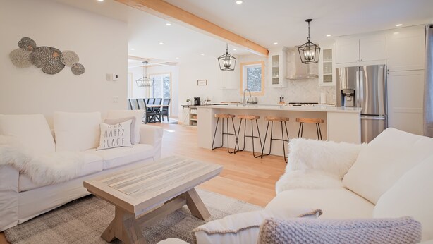 Un salon moderne avec un canapé blanc, une table basse en bois et un coin cuisine doté de meubles blancs et d’appareils électroménagers en acier inoxydable.