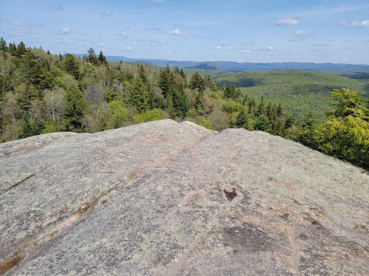 A large rock formation with a view of a forested mountain range in the background.