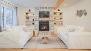 Un salon moderne avec une cheminée, deux canapés blancs, une table basse et un mur en pierre.