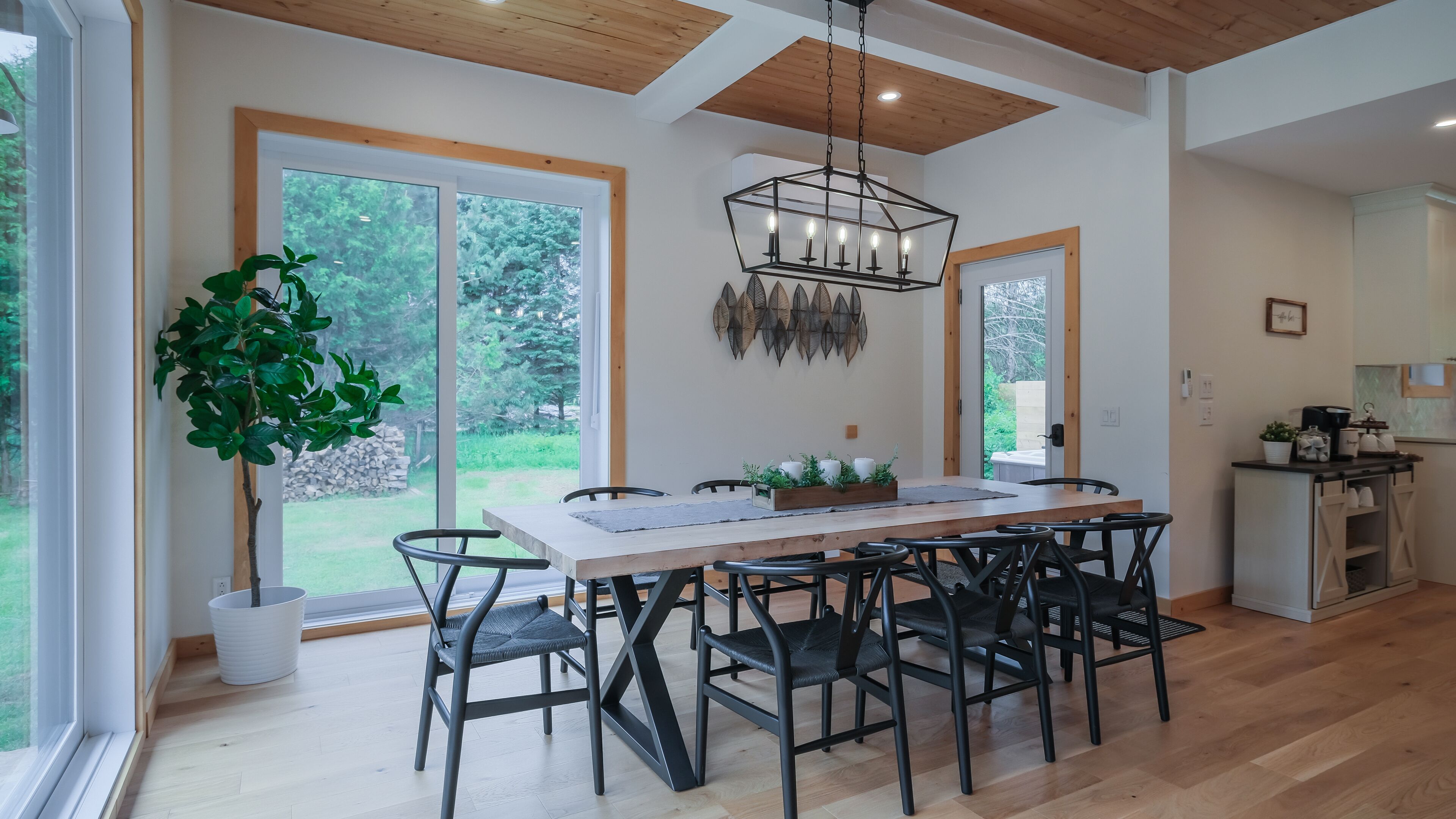 A modern dining area with a wooden table and chairs, large windows, and a hanging light fixture.