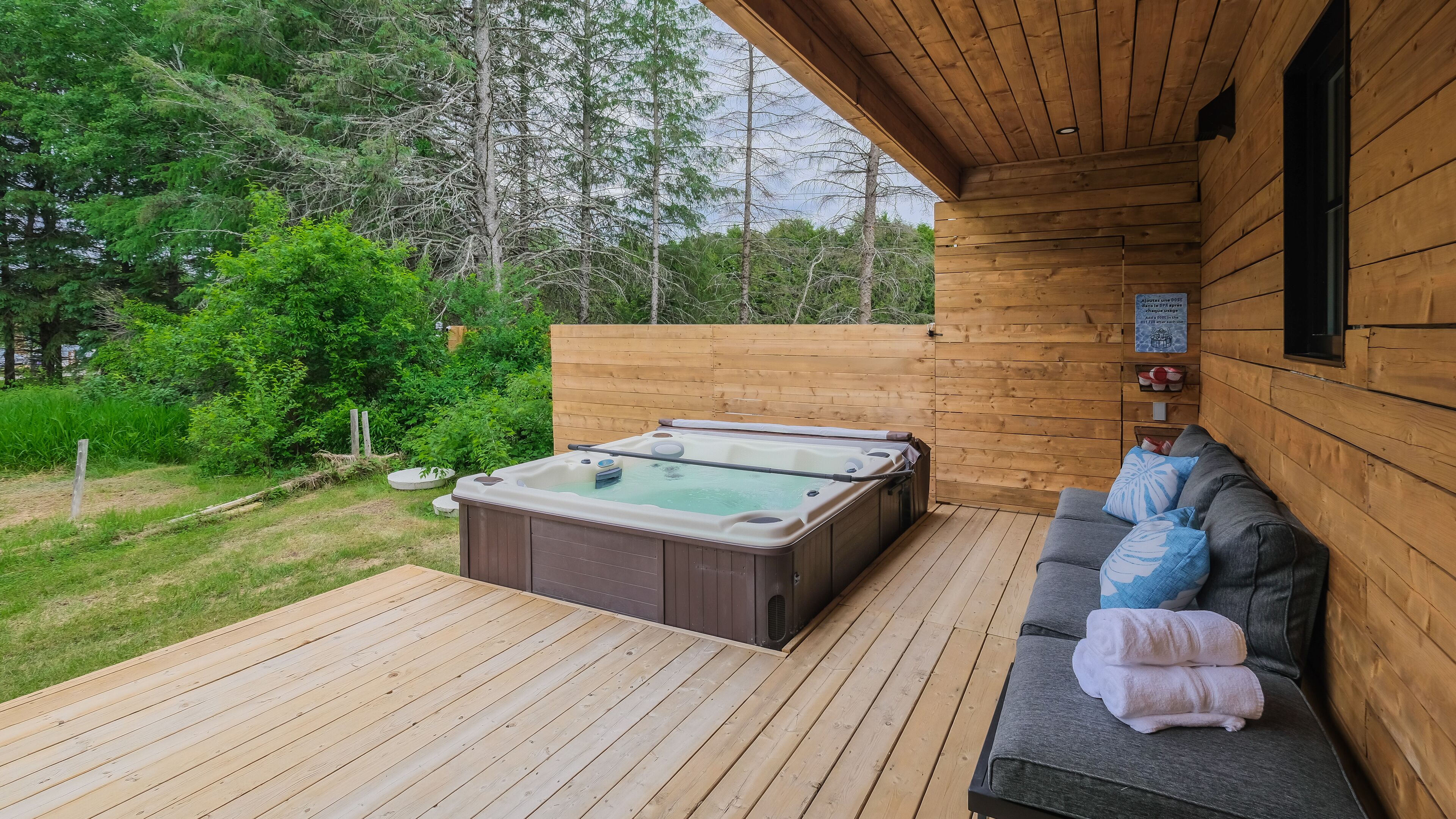 Una terrazza in legno con una vasca idromassaggio e un divano con asciugamani.