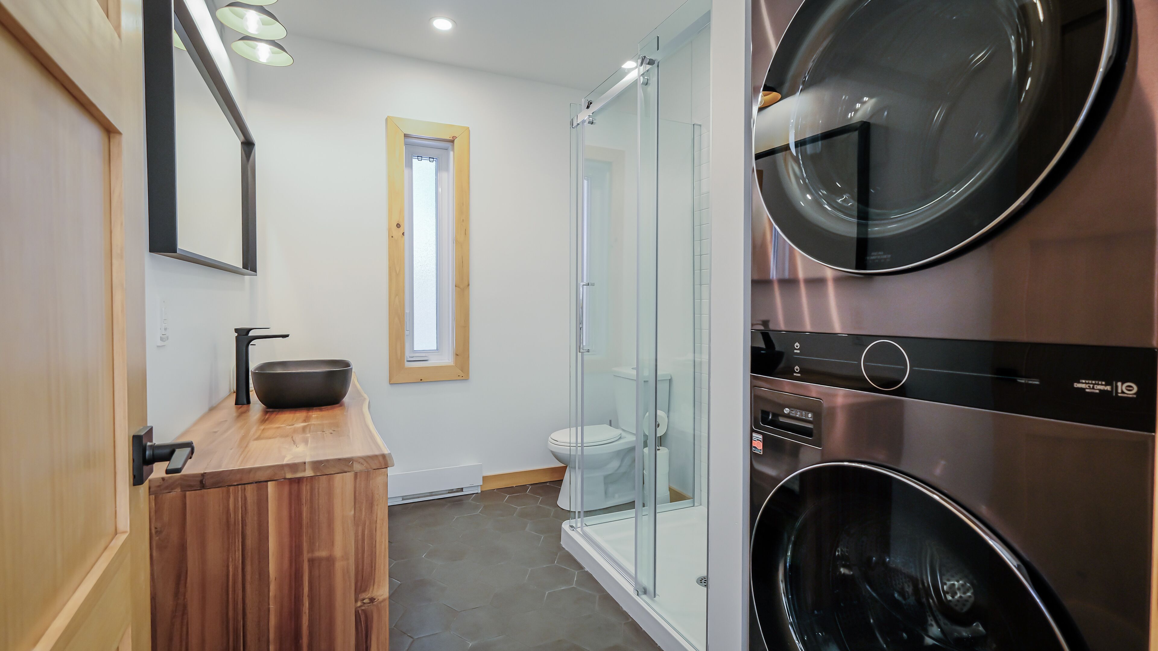 A modern bathroom with a wooden vanity, a glass shower enclosure, and a built-in washer and dryer.