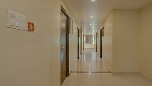 Un pasillo de hotel con suelo de baldosas, puertas y un interruptor de luz en la pared.