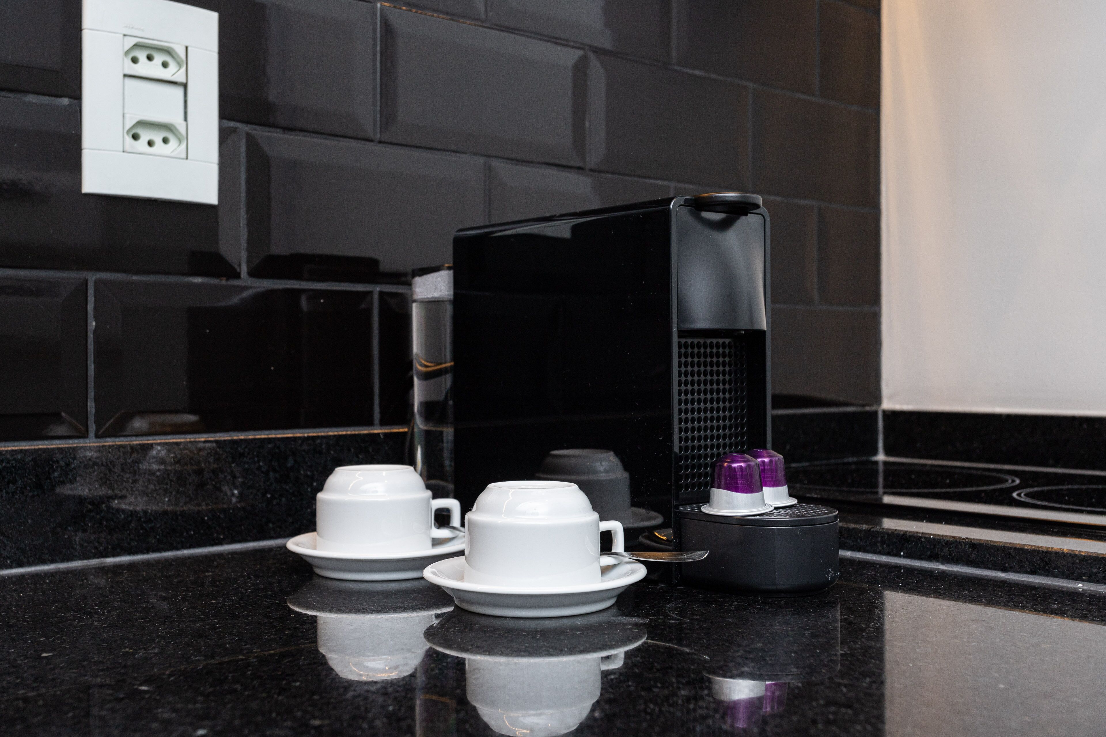 A modern kitchen with black countertops, a coffee machine, and a set of white cups and saucers.