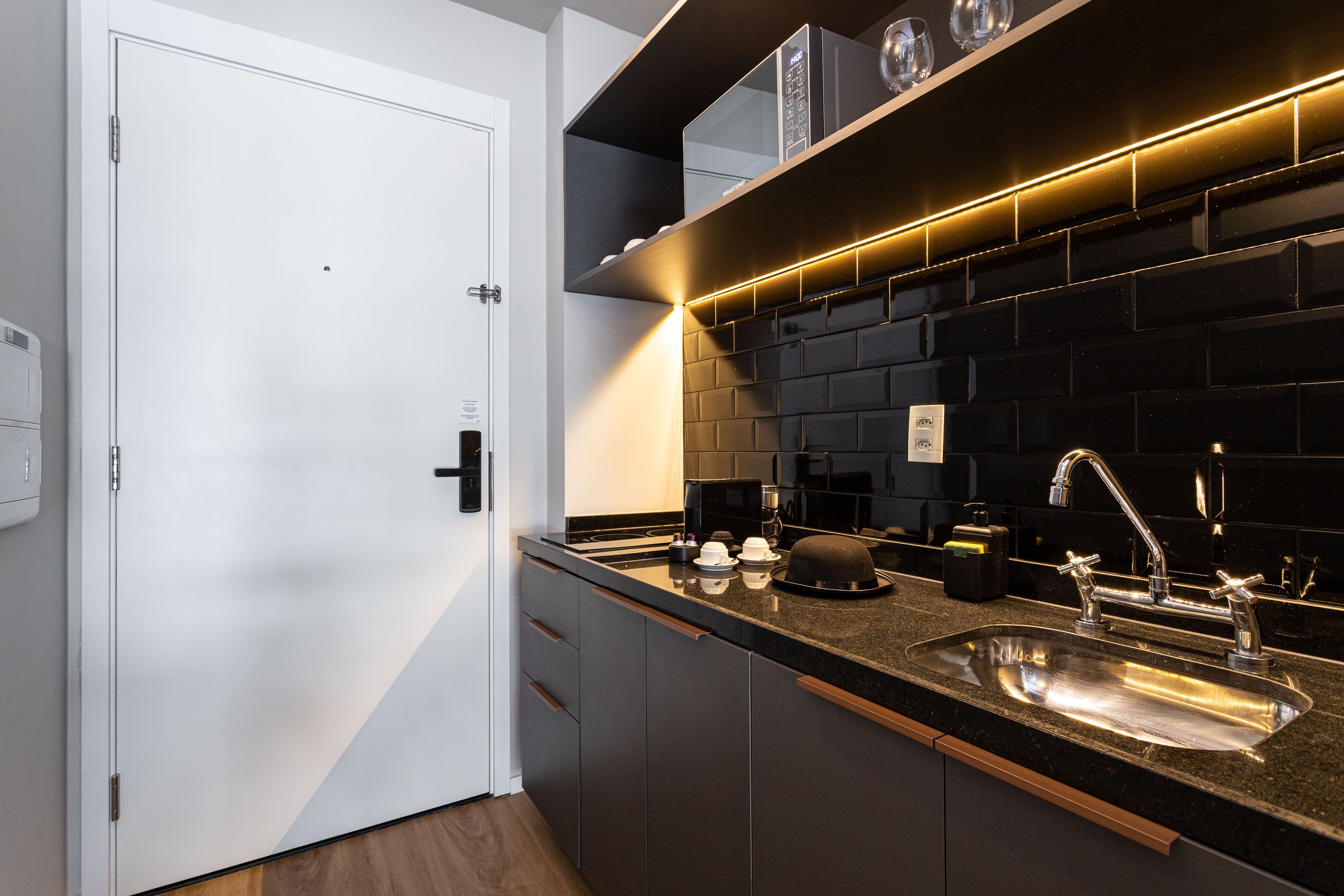 Una cocina moderna con un protector contra salpicaduras negro, un lavamanos de acero inoxidable y una puerta blanca.