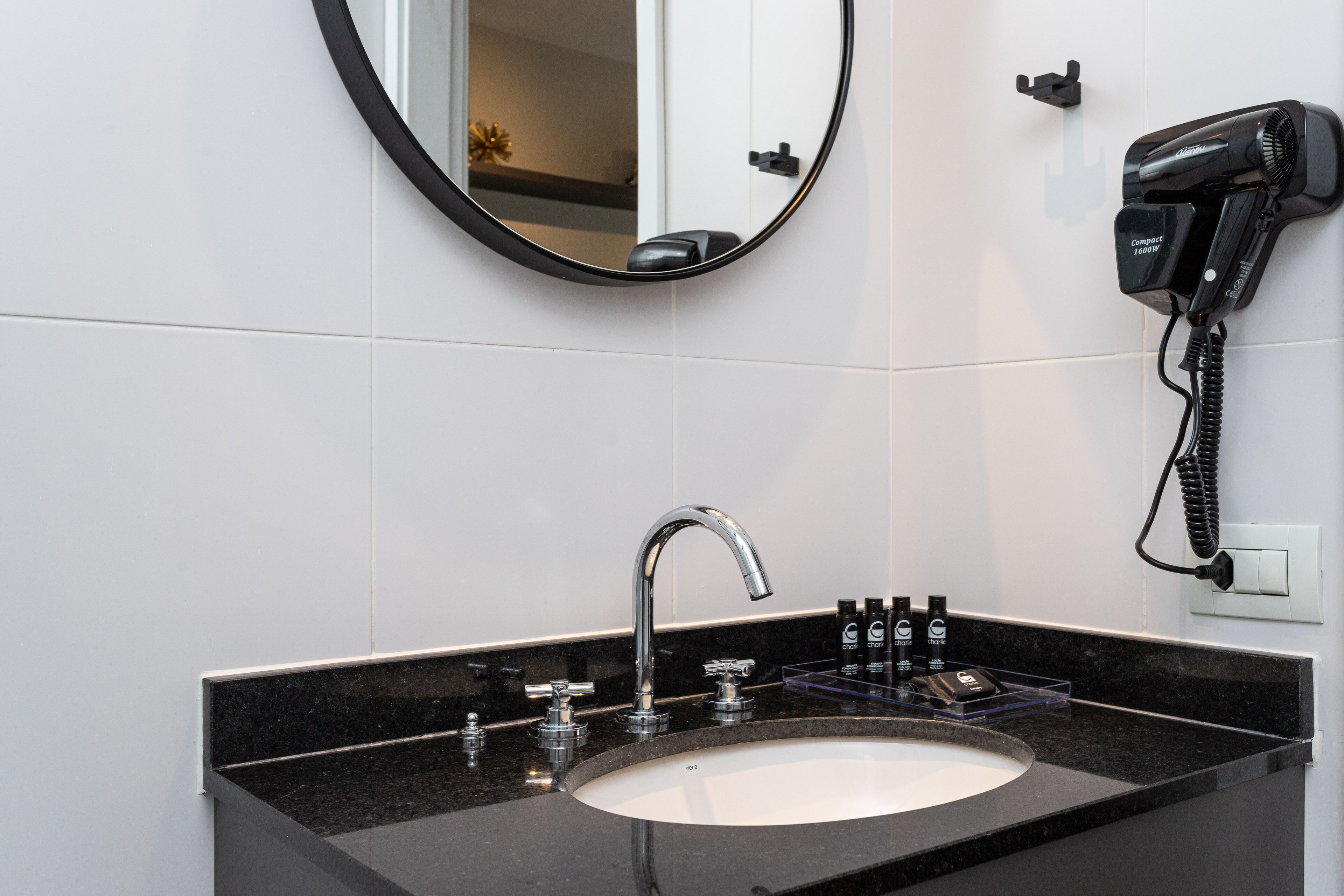 Une salle de bain avec un lavabo au comptoir noir, un robinet moderne et un sèche-cheveux fixé au mur.