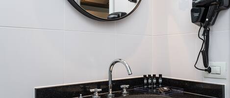 A bathroom with a black countertop sink, a modern faucet, and a hairdryer mounted on the wall.