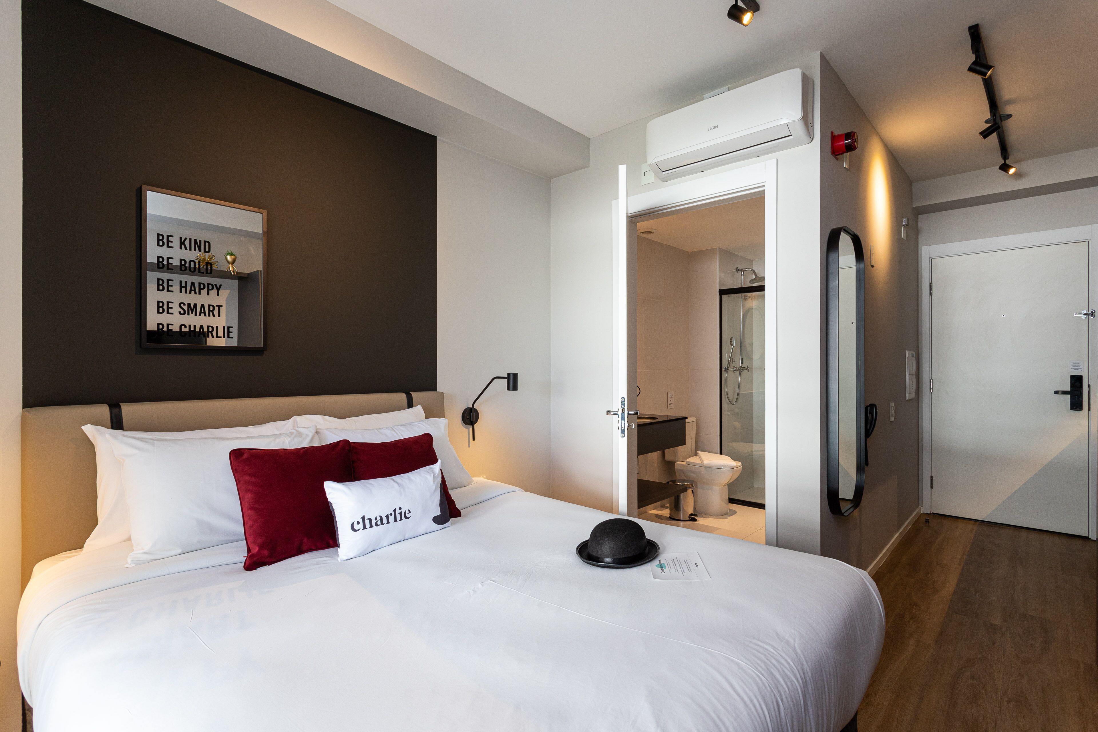 A hotel room with a bed, a motivational quote on the wall, a mirror, and a bathroom visible through an open door.