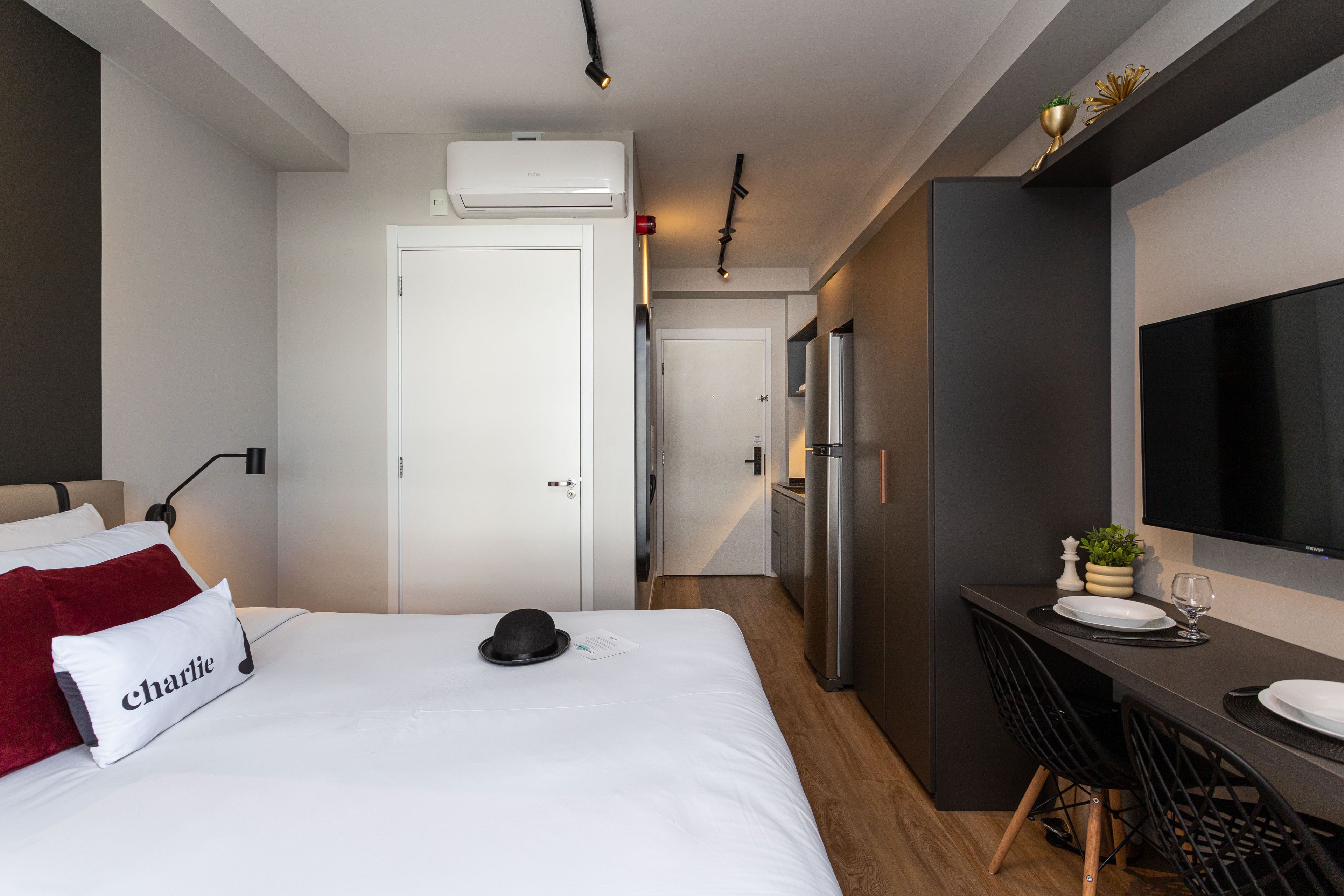 A modern hotel room with a bed, a desk, a flat-screen TV, and a kitchenette.
