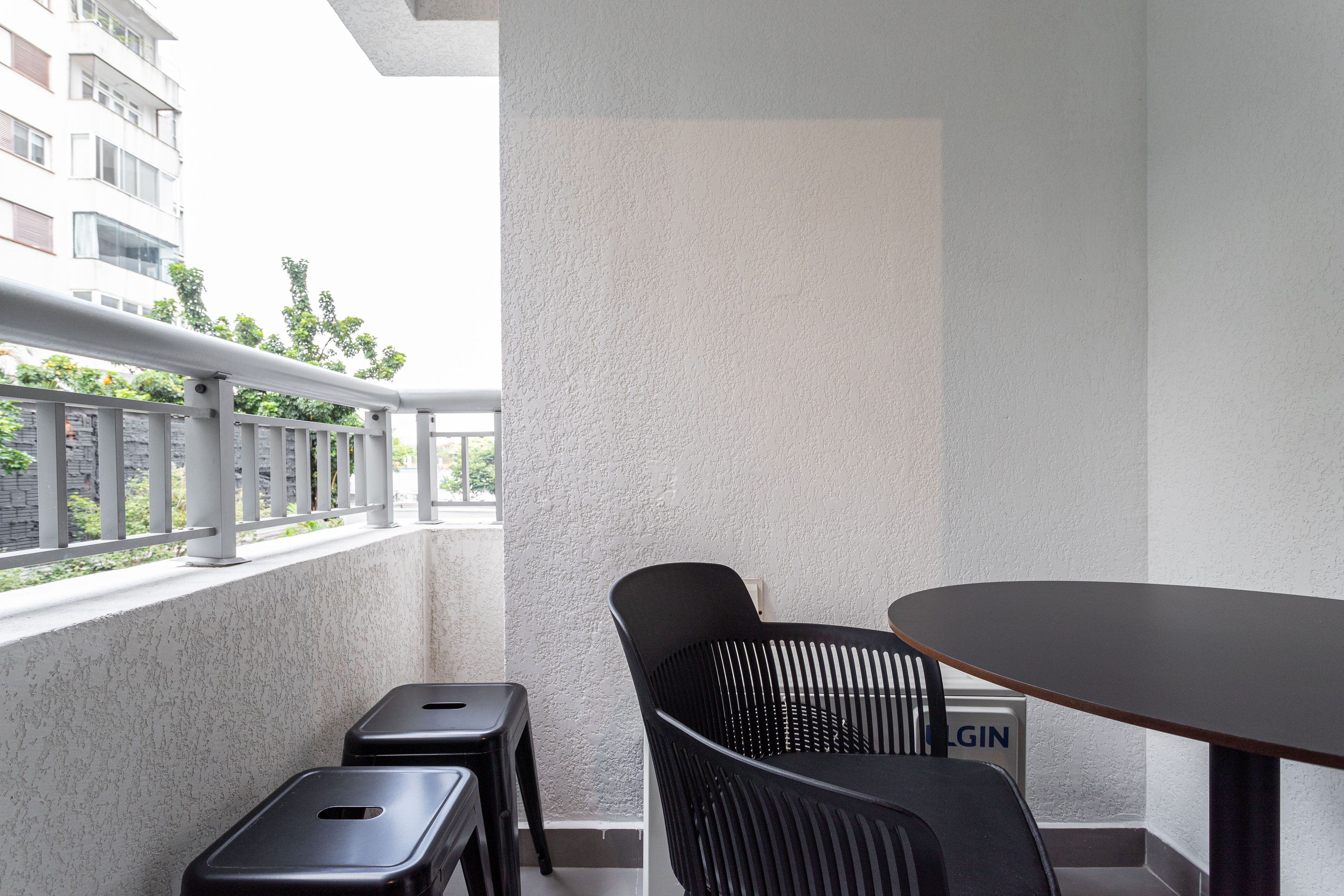 A balcony with a white textured wall, a metal railing, a black chair, a small table, and a sign with "LOGIN" on it.
