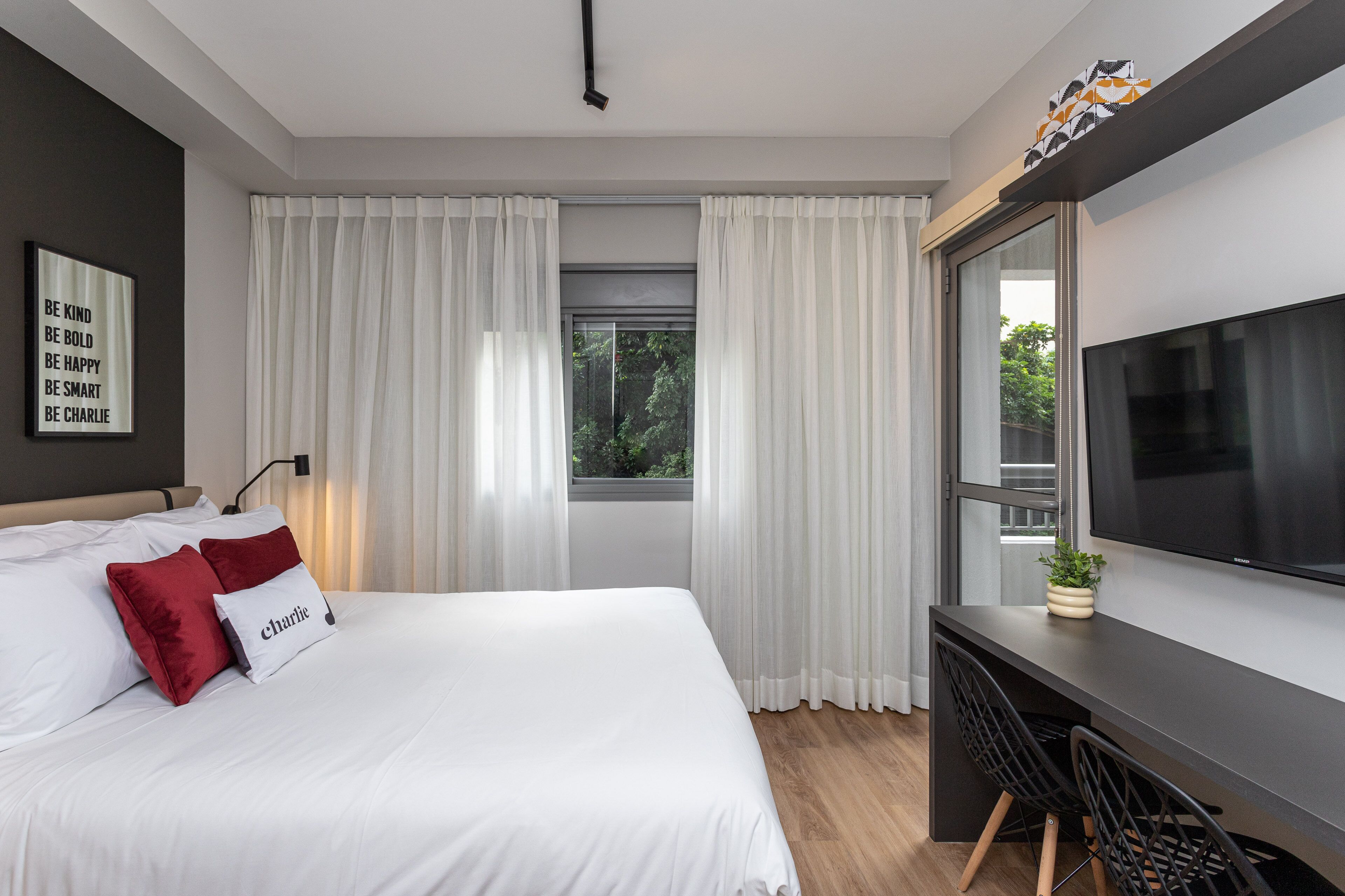Una habitación de hotel moderna con una cama grande, un escritorio con dos sillas, un televisor y una ventana con cortinas.
