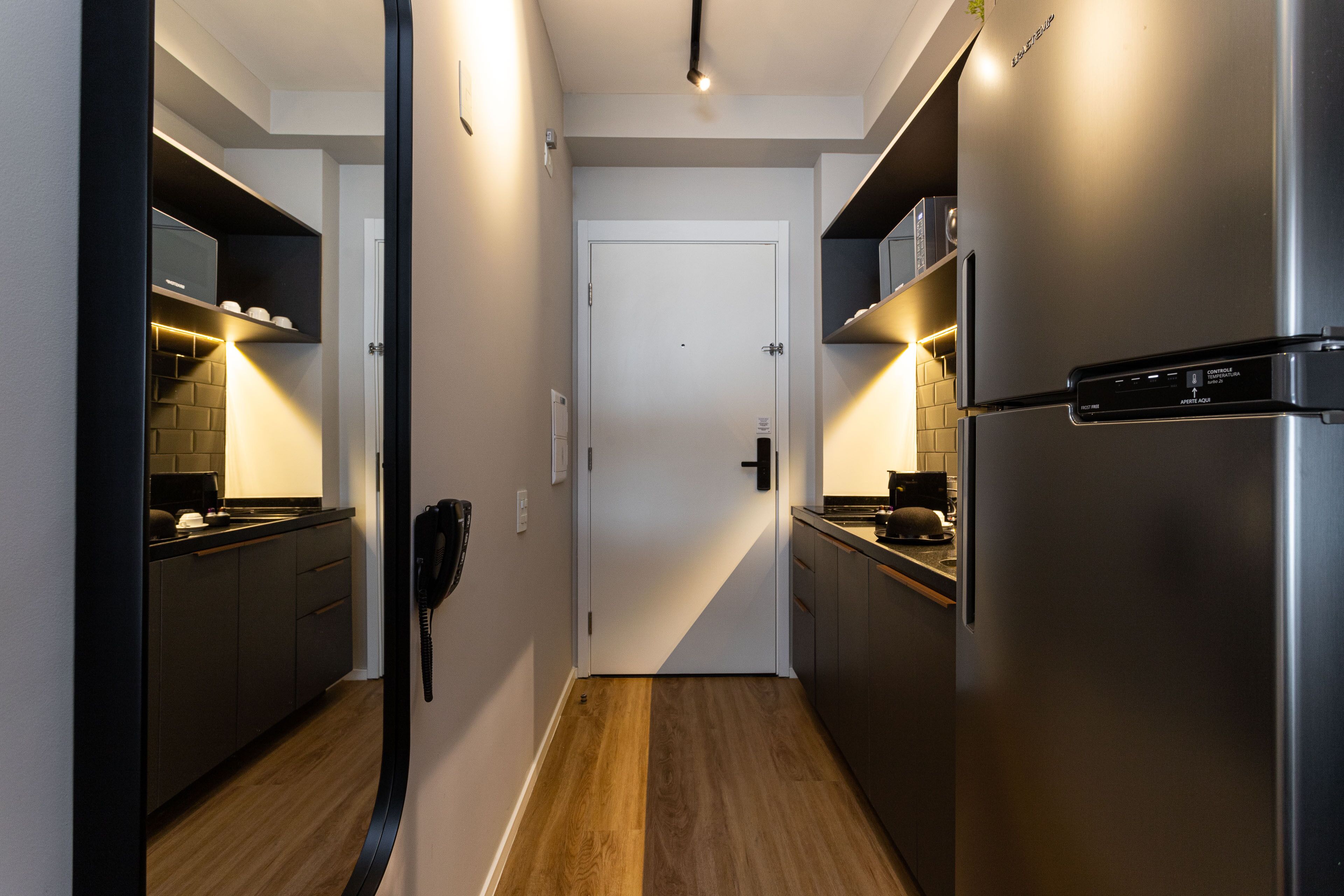 Eine schmale Küche mit Kühlschrank, Mikrowelle und Kaffeemaschine auf der Arbeitsplatte.