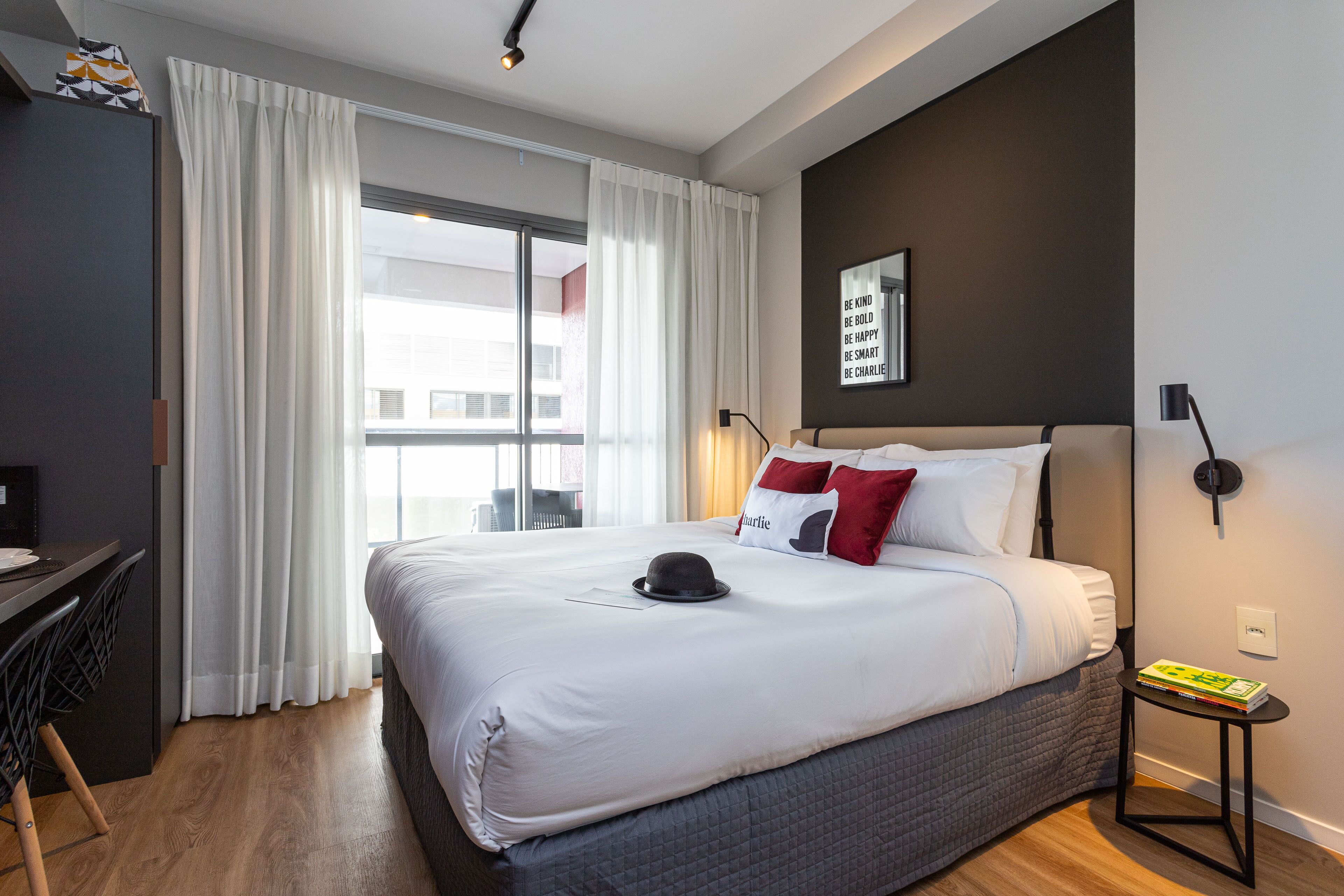 A modern hotel room with a large bed, a desk, and a view of the city.
