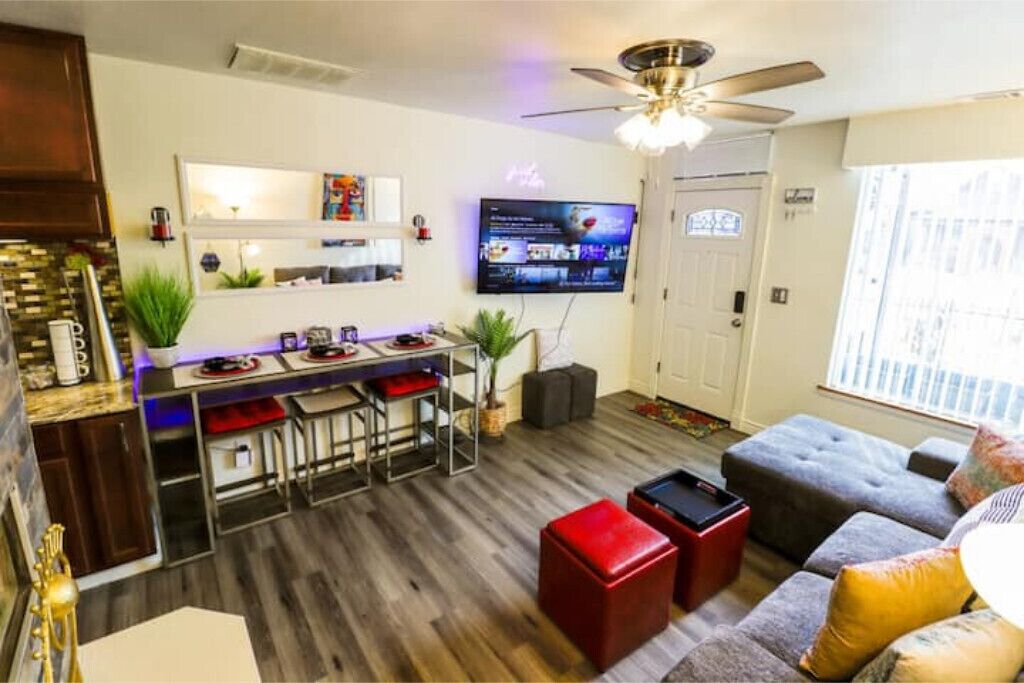 Una sala de estar moderna con un sofá gris, un otoman rojo y un televisor montado en la pared.