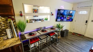 A modern kitchen with a bar area, a flat-screen TV mounted on the wall, and a wooden floor.