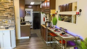 A modern kitchen with wooden cabinets, a central island, and a dining area with a long table.