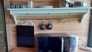 A kitchen area with wooden walls, a microwave, a coffee maker, and a shelf with kitchen utensils. - Cosy Cabin Near Seljalandsfoss (Rangárþing eystra)