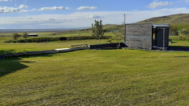 A small, single-story building with a sloped roof, situated in a grassy field with a clear sky. - Cosy Cabin Near Seljalandsfoss (Rangárþing eystra)
