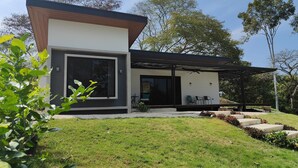 Uma casa moderna com uma grande janela, um pátio com mobiliário exterior e um gramado bem cuidado.