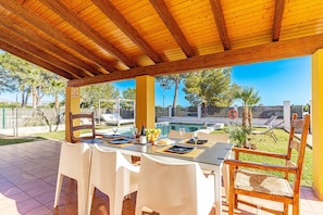 An outdoor patio with a wooden pergola, a dining table set with white chairs, and a pool in the background. - Villa Ibiza 350m from the beach, swimming pool, billiards and table tennis. (Alcúdia)