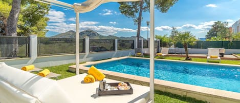 Uma área na piscina com um espaço de estar coberto, piscina e vista para as montanhas.