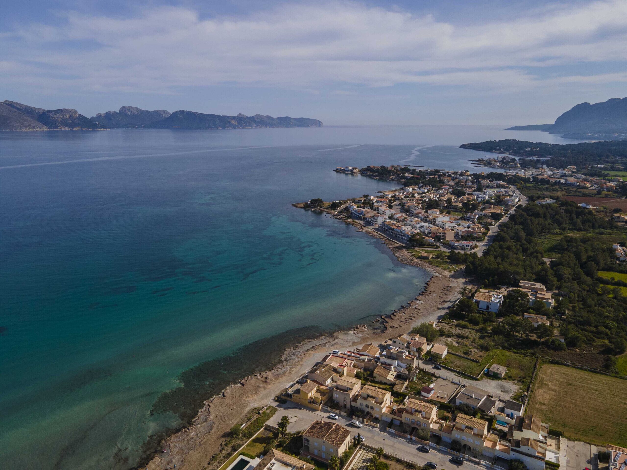 An aerial view of a coastal town with a clear view of the coastline, residential buildings, and a small harbor.