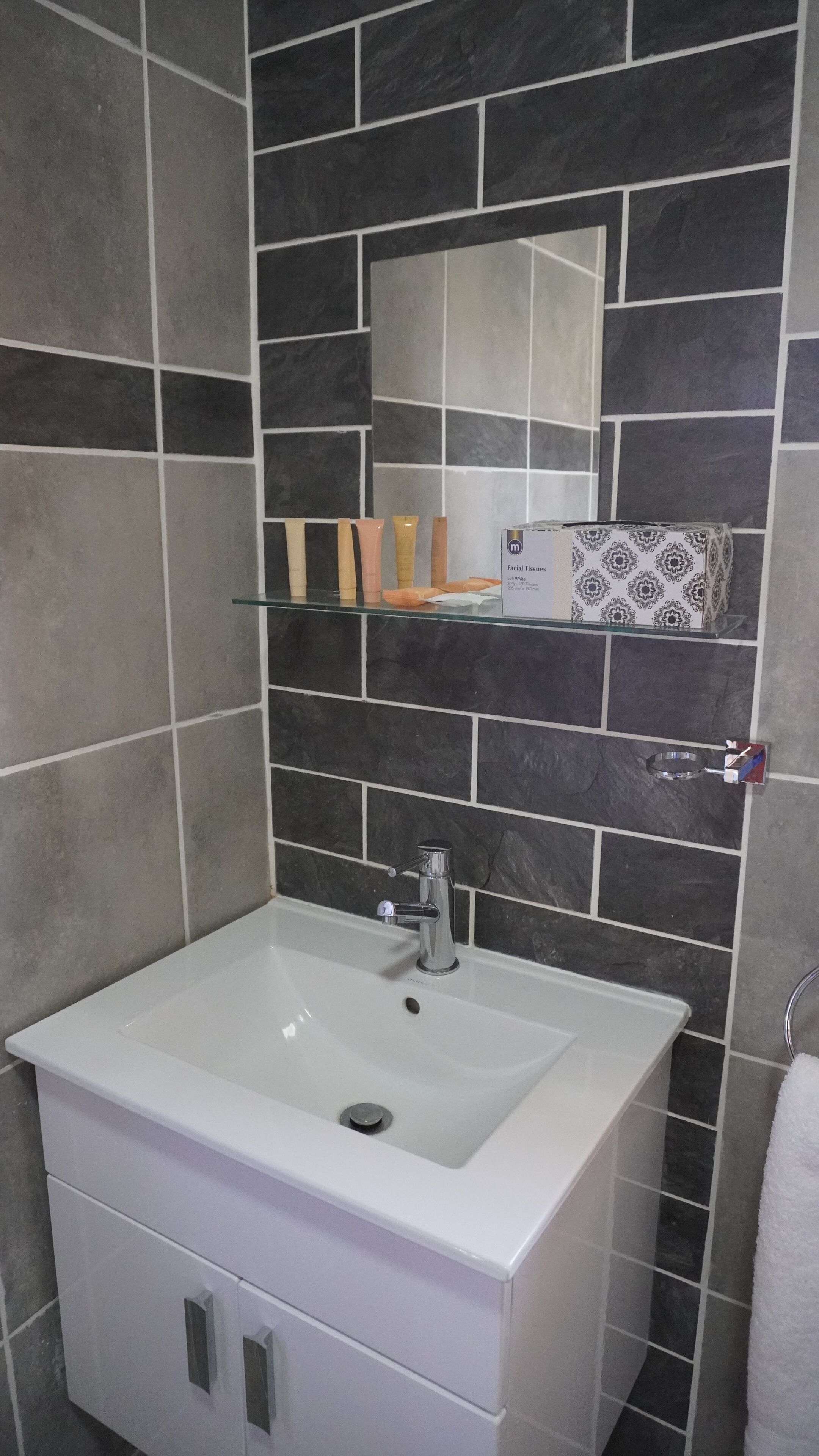 A bathroom with a white sink, a mirror, and a shelf with toiletries.