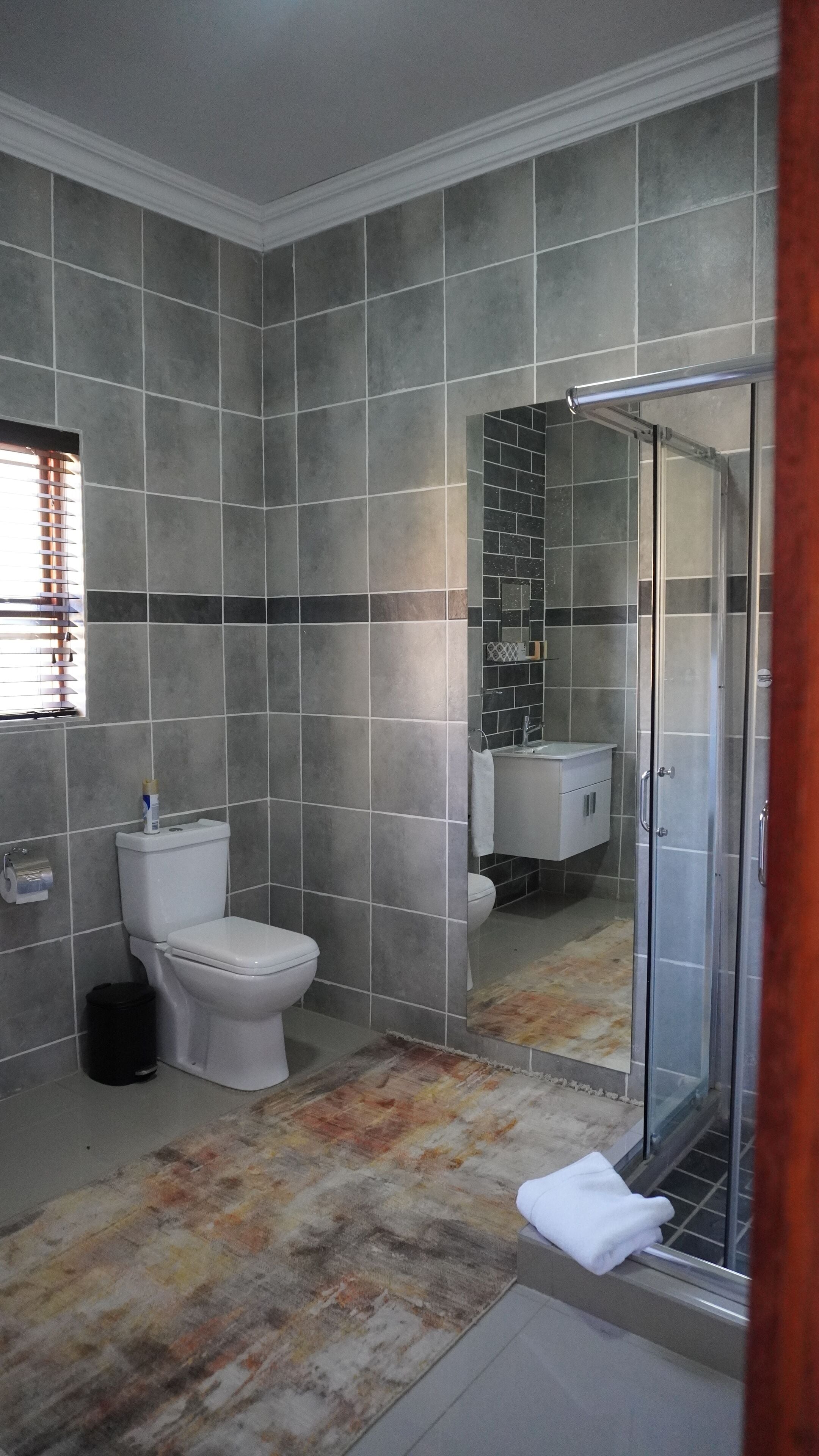 Un baño con inodoro, ducha con puerta de vidrio y lavamanos con espejo.
