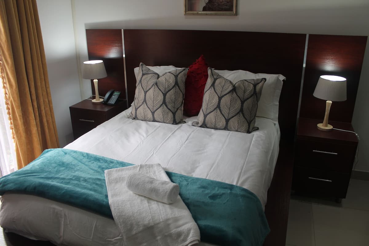 Une chambre d’hôtel comprenant un lit, deux tables de chevet, une commode, une lampe, un téléphone et une fenêtre avec des rideaux.