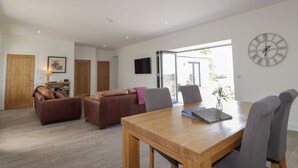 A spacious living area with a wooden dining table, two sofas, and a large window providing a view of the outside. - Firthview (Nairn)
