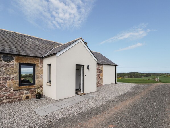 A stone building with a white facade, a gravel driveway, and a view of the countryside.