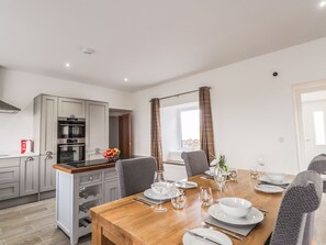 A modern kitchen with built-in appliances and a dining area with a wooden table set for four.