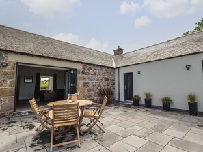 A stone building with a tiled patio, a round wooden table, and folding chairs.