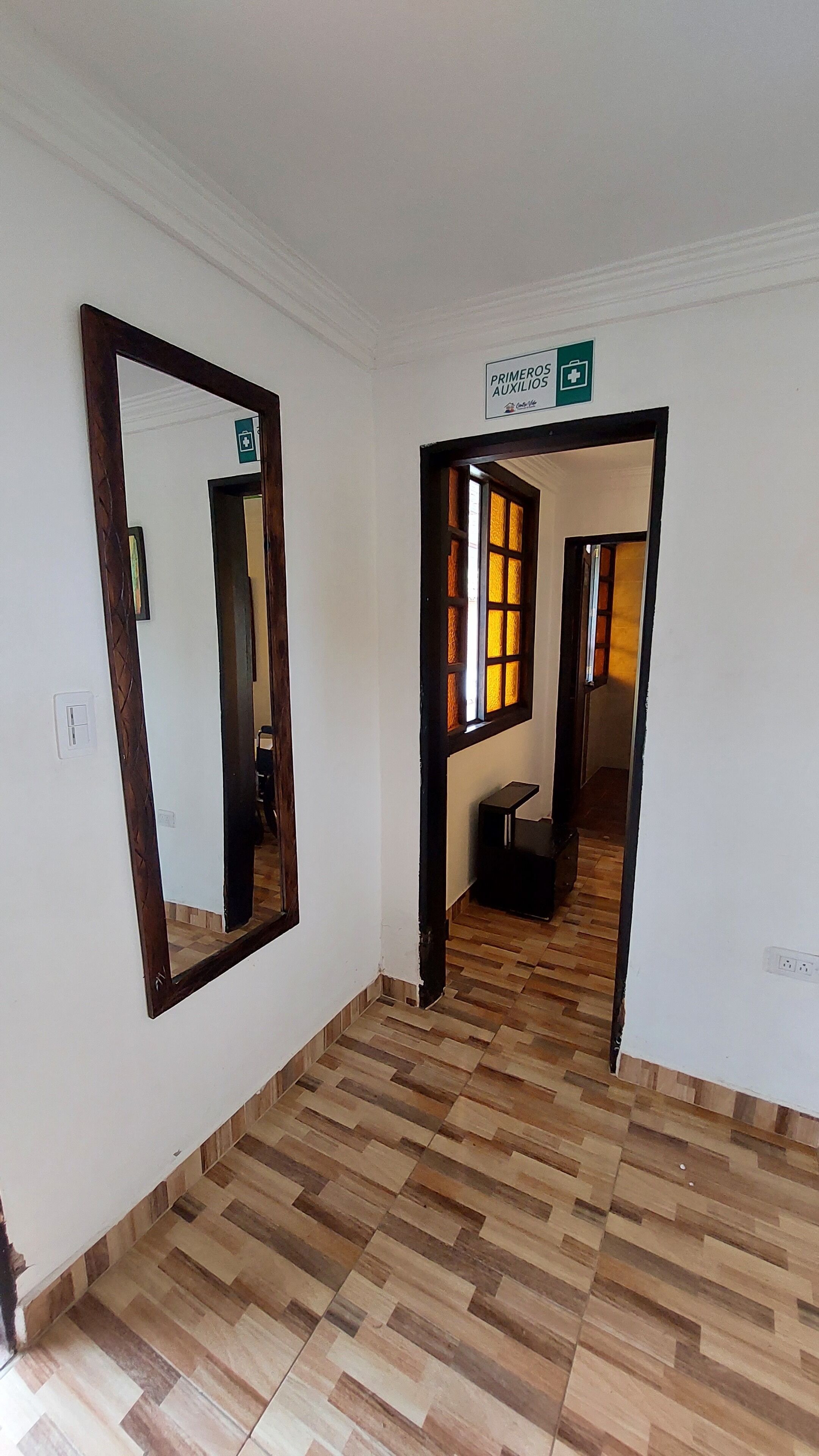 A hallway with a wooden floor, a large mirror, and a sign indicating first aid assistance.