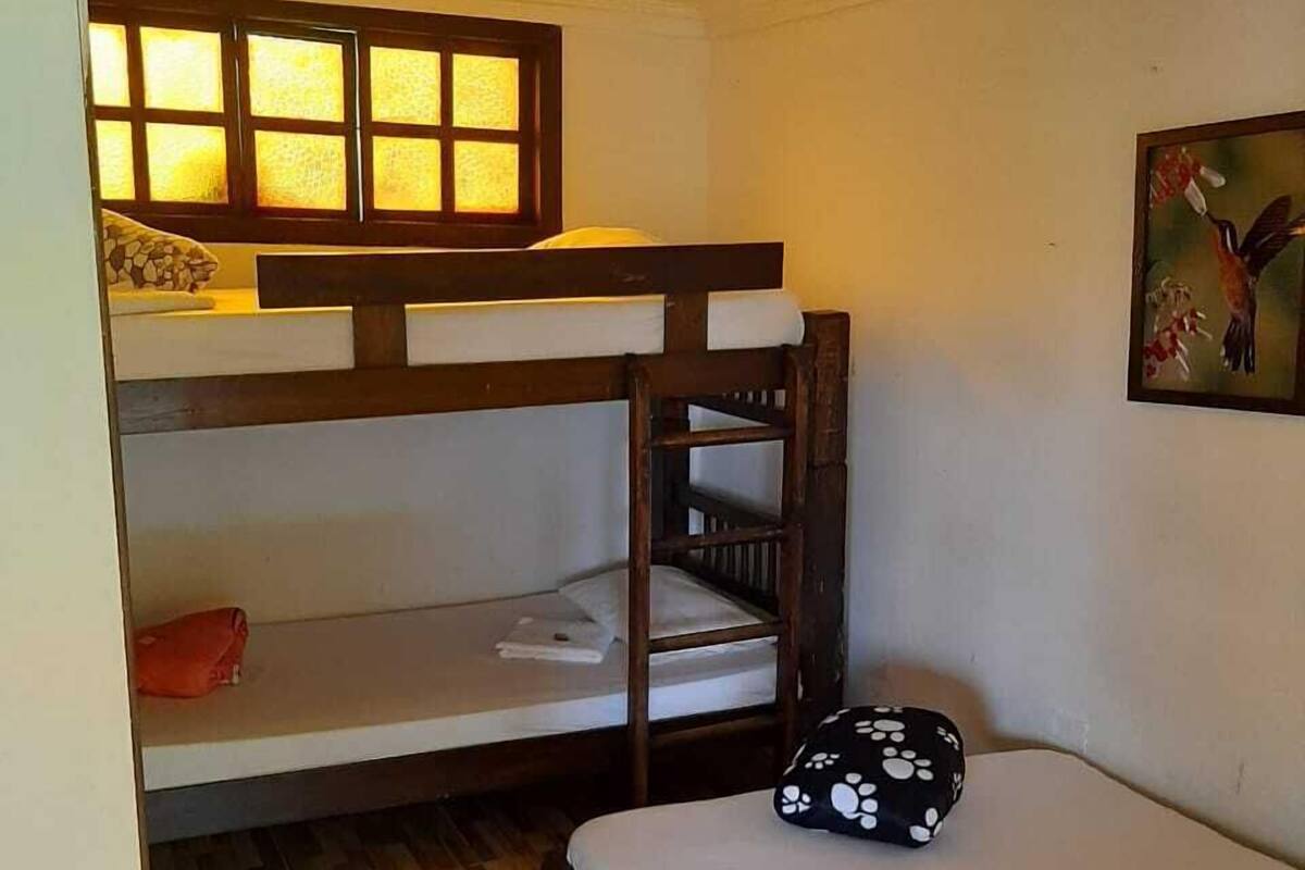 A dormitory room with bunk beds, a wooden floor, a ceiling fan, and a painting on the wall.