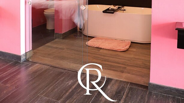 A modern bedroom with a glass door leading to a bathroom. The room features a bed, a bedside table, and a large mirror. The bathroom includes a bathtub and a toilet.