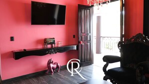 A room with a red wall, a black TV mounted above a console table, a chandelier, and a large ornate chair.