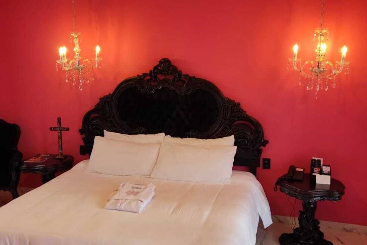 Ein Zimmer mit einem großen Bett, zwei Nachttischen, einem Sessel und einer Kristallleuchtre.