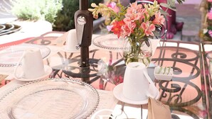 A glass-top table with a menu, a vase of flowers, and a decorative metal sculpture in a courtyard setting.