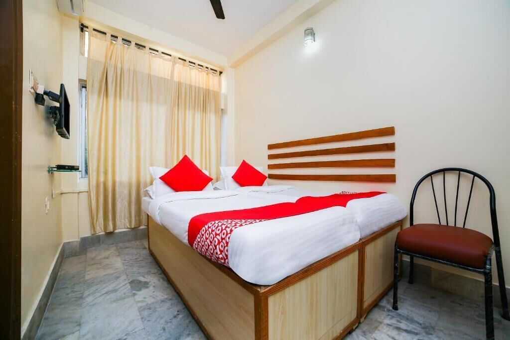 Una habitación de hotel con cama, una silla, televisor y cortina.