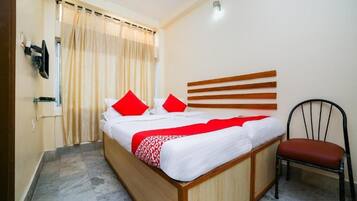 Una habitación de hotel con cama, una silla, televisor y cortina.