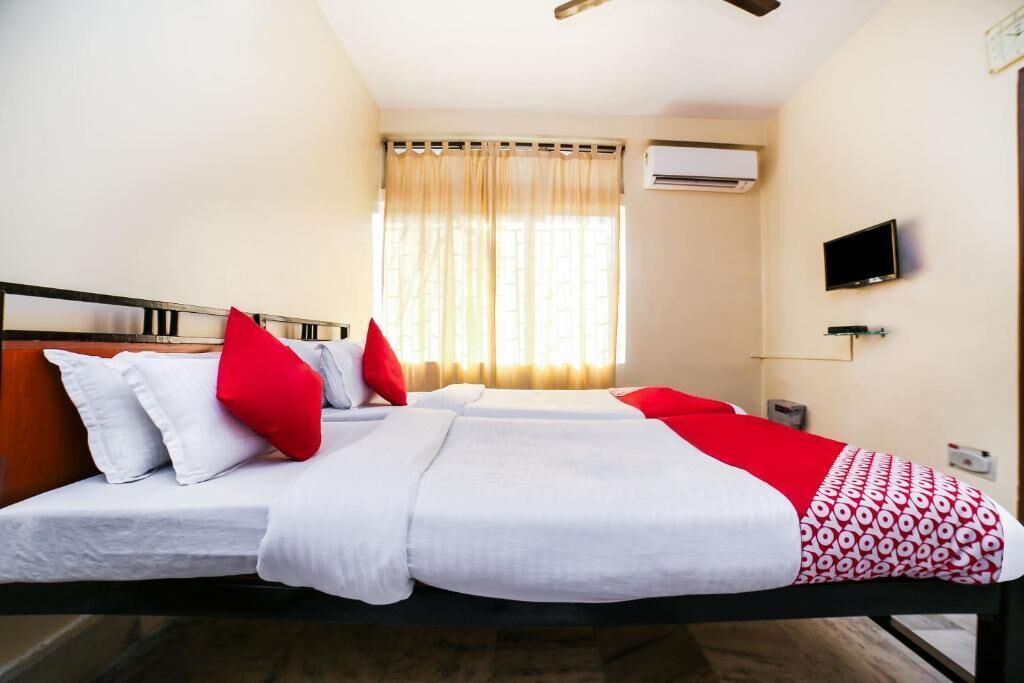 A hotel room with two beds, a TV, an air conditioner, and a window with curtains.