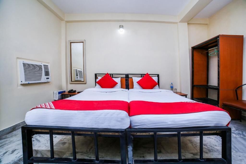 Een tweepersoonsbed met rode en witte beddengoed, een houten garderobe en een airconditioningsunit aan de muur.
