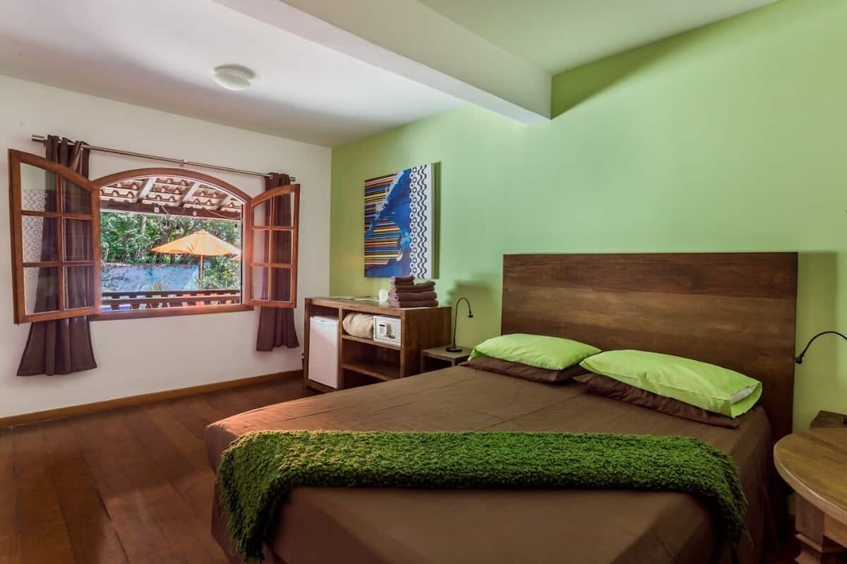 A bedroom with a bed, a desk, and a window with curtains.