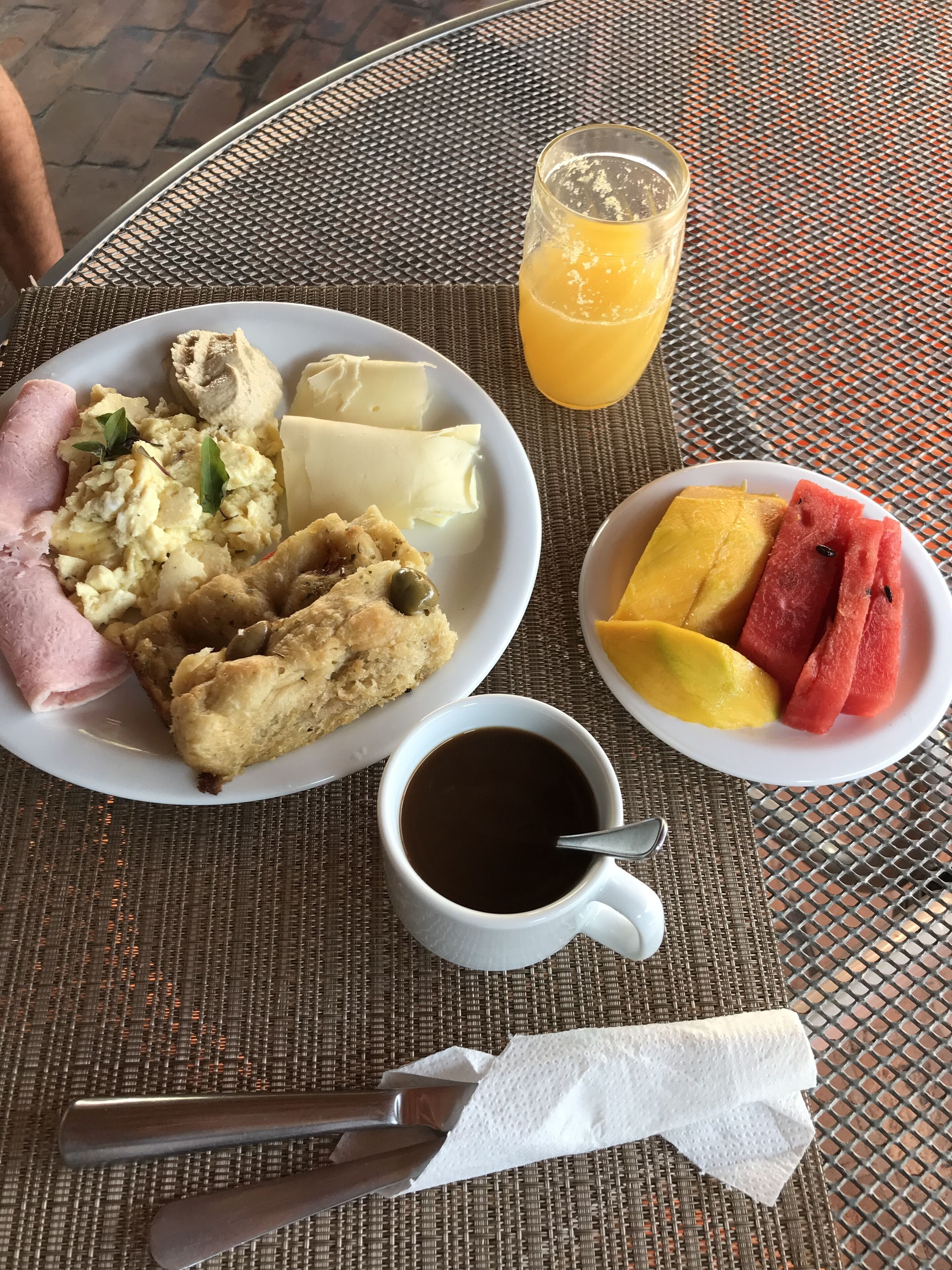 Ein Essen mit Rührei, Schinken, Gebäck und einem Glas Orangensaft auf einem gewebten Tisch.