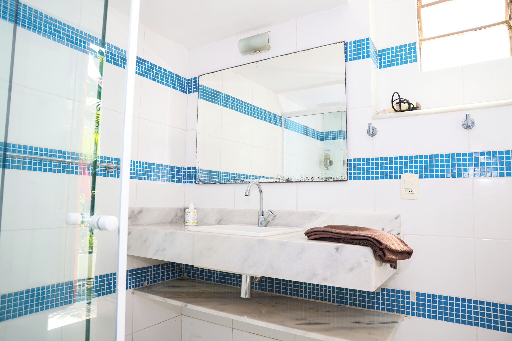A bathroom with a white sink, blue-tiled walls, a mirror, and a towel.