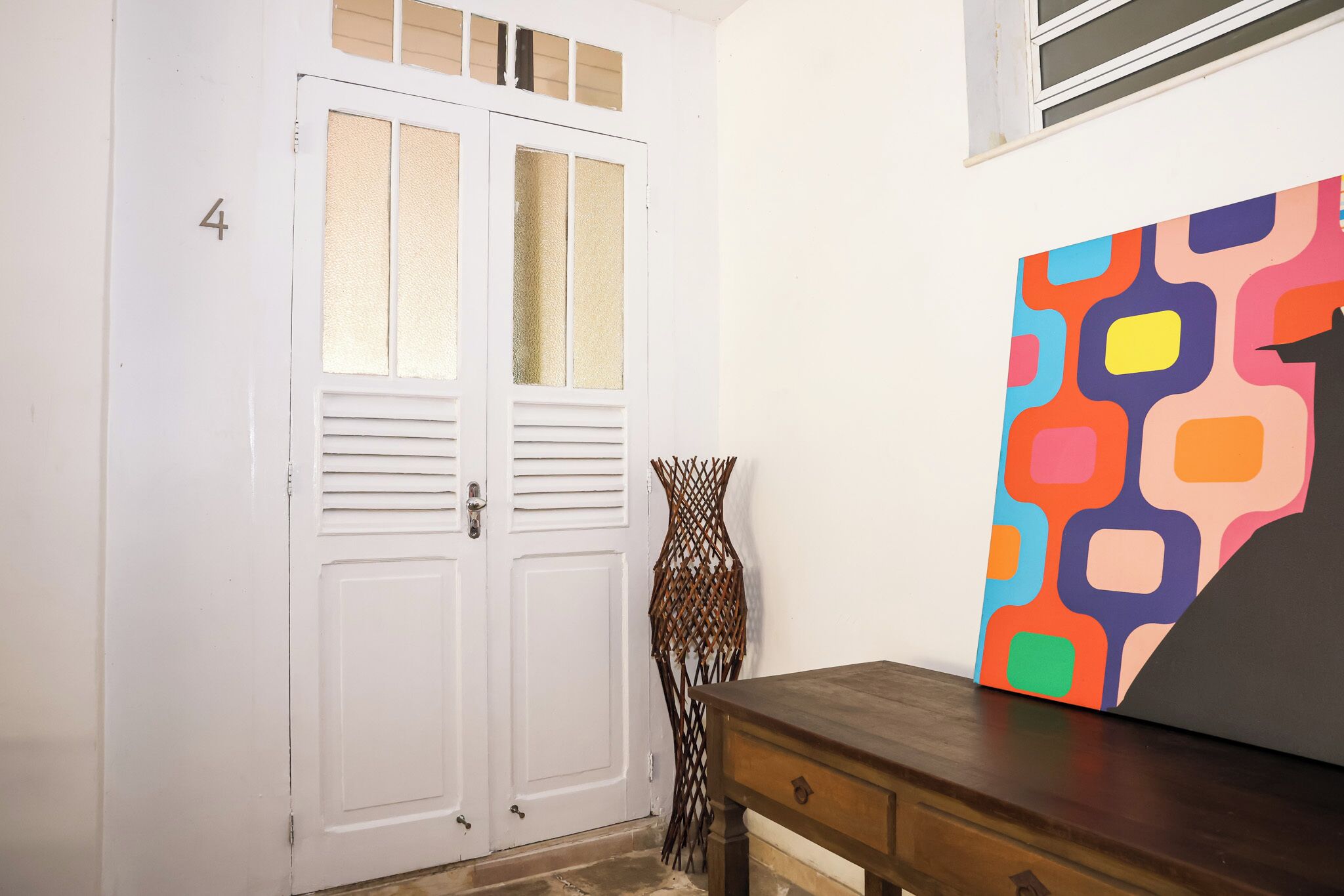 A white door with a number '4' on the wall, a wooden table, and a colorful abstract painting.